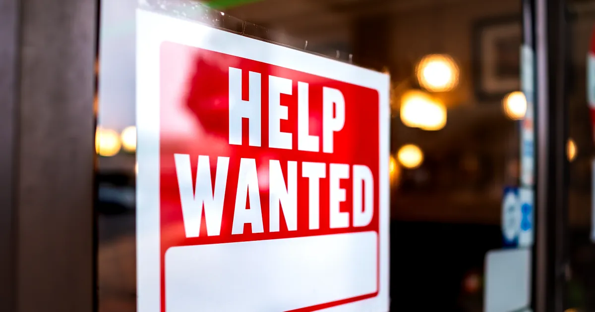 A help wanted sign on a store window showing how labor shortages are impacting the future of supply chain. 